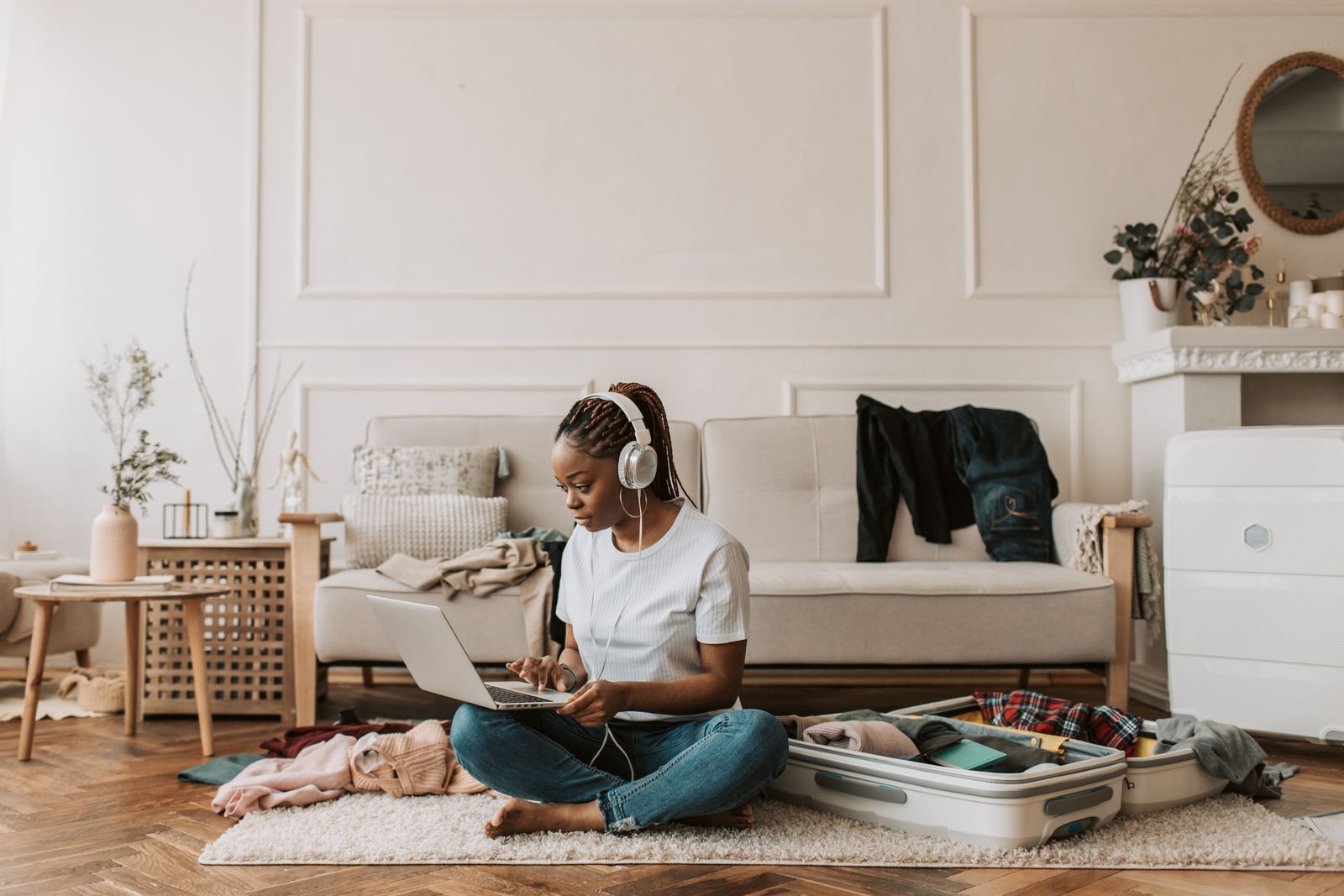 Woman working on a laptop at home beside a packed suitcase — part-time travel agent